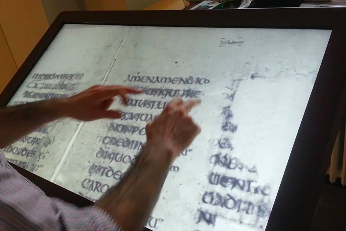 Il Metaleggio del Codex: mani sfogliano sul touch screen le pagine con la scrittura del manoscritto