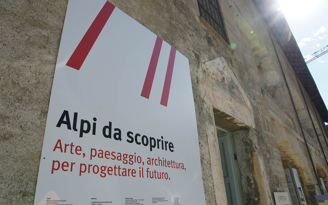 Manifesto della mostra Alpi da scoprire affisso su muro in pietra