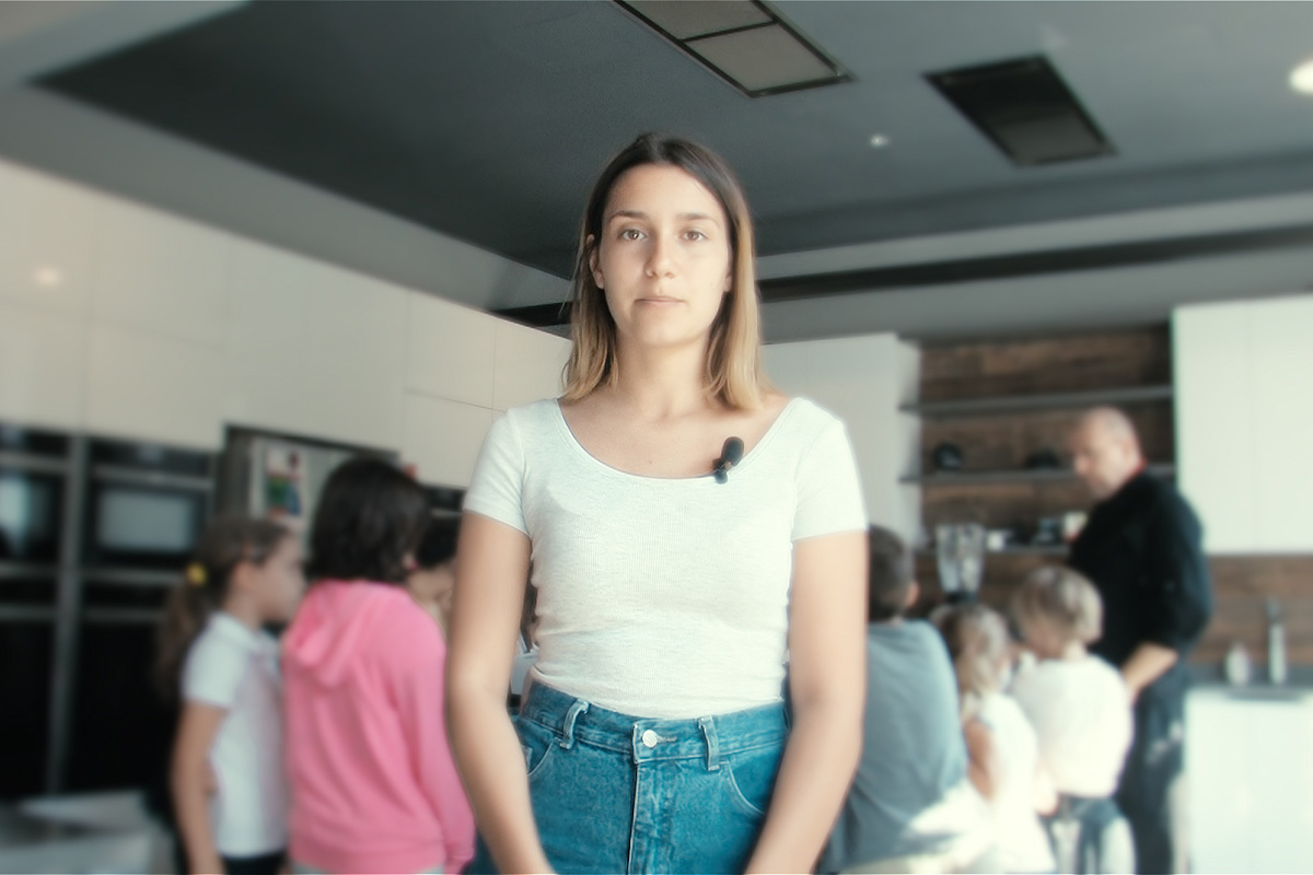 Ragazza con microfono lavalier davanti alla camera, bambini sullo sfondo in cucina