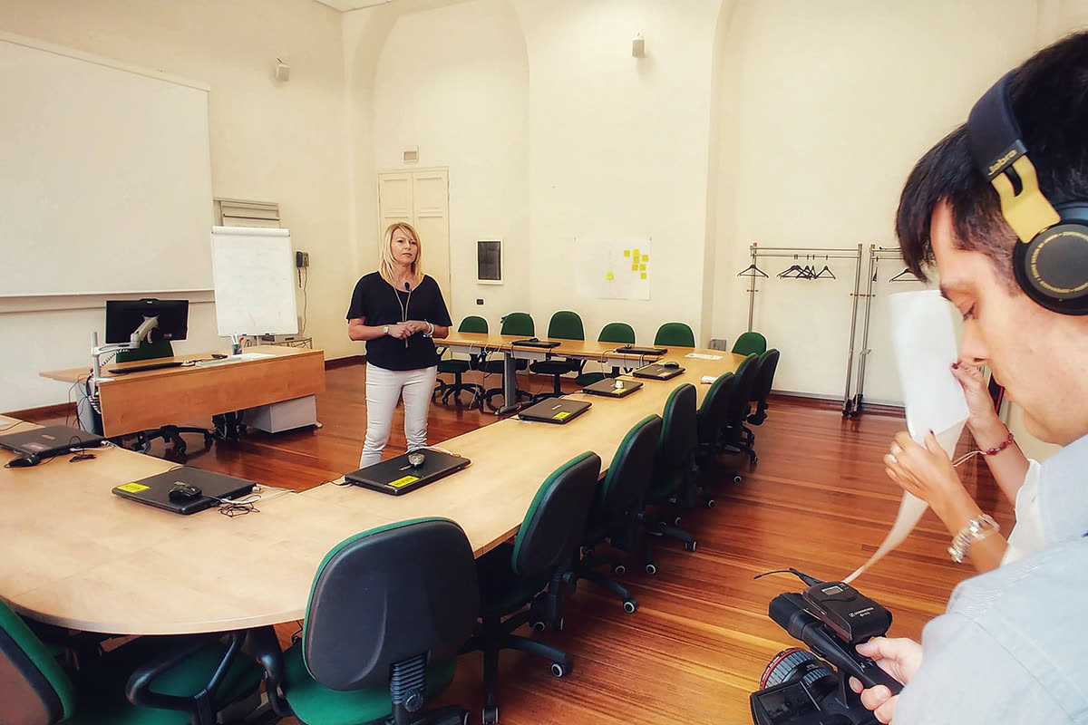 Cameraman con cuffie riprende una donna in una sala riunioni