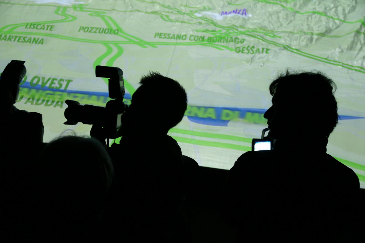 Visitatori in controluce fotografano la mappa delle tangenziali proiettata sul plastico