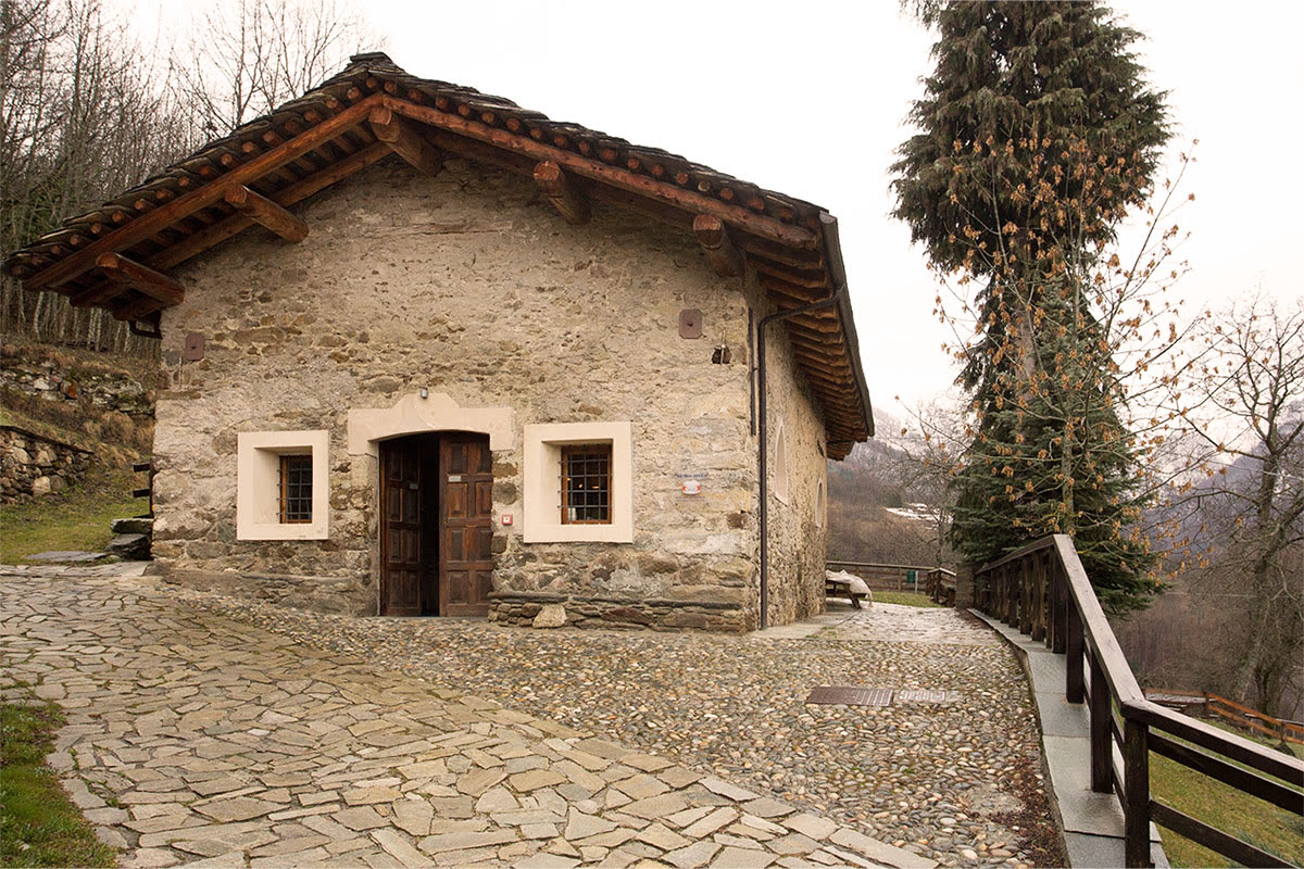 Antico edificio in pietra con tetto in legno e cortile in acciottolato, sede museale alpina