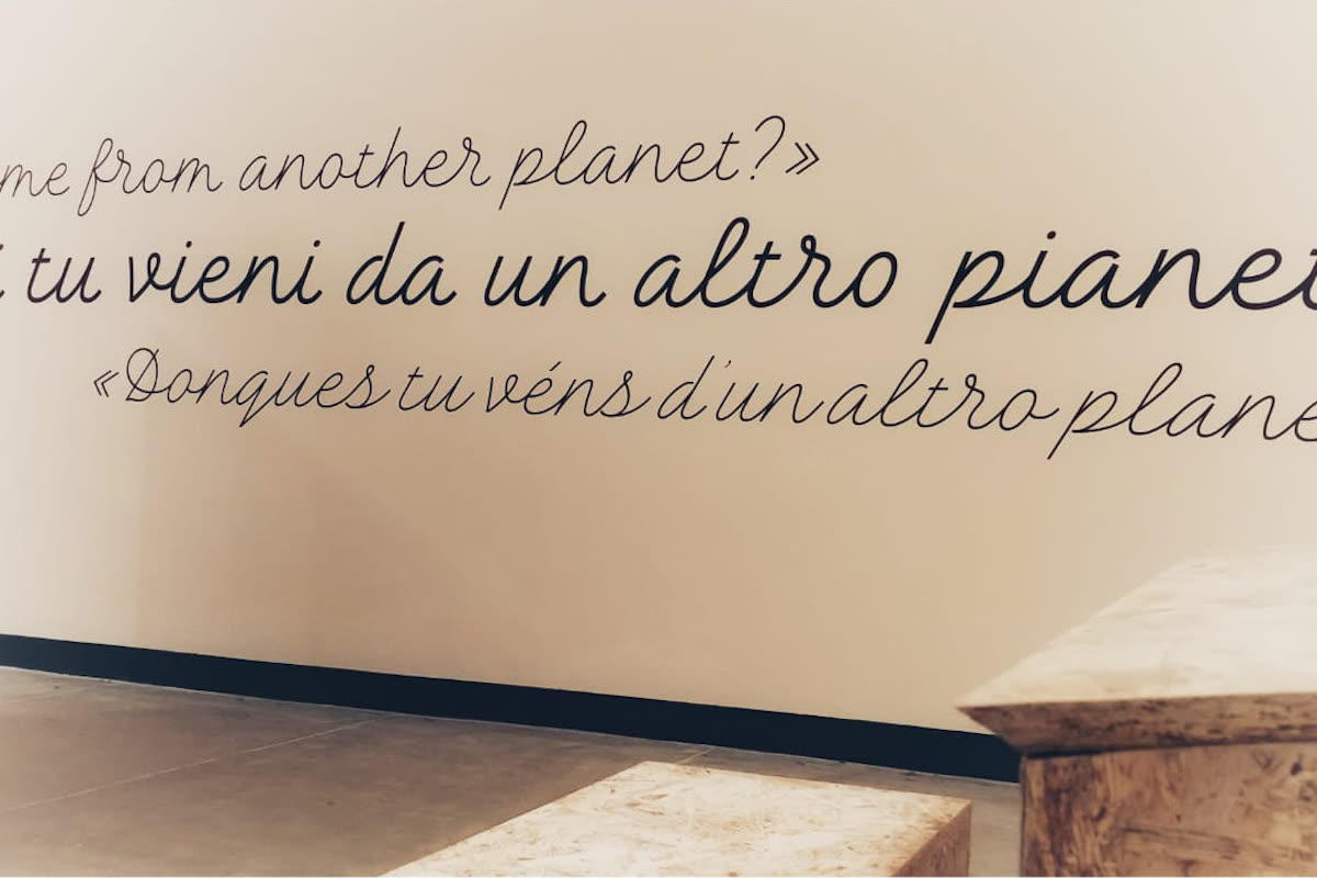Citazione del Piccolo Principe in corsivo multilingue sulla parete con sedute in OSB