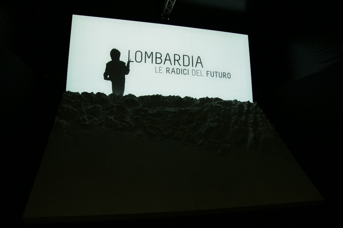Plastico al buio con schermo verticale "Lombardia Le radici del futuro" e silhouette