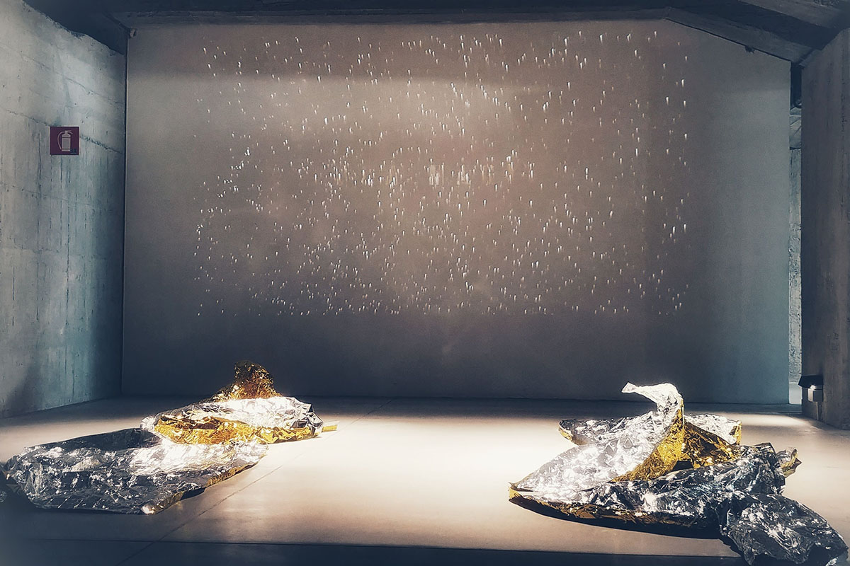 Coperte isotermiche oro e argento accartocciate a terra sotto una proiezione stellata