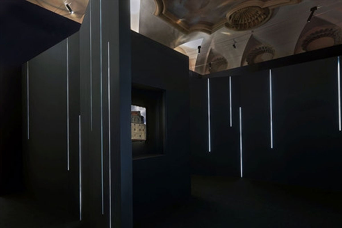 Sala buia con linee luminose verticali e plastico dell'abbazia in nicchia illuminata