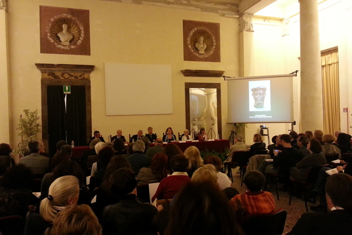 Conferenza nella sala di Palazzo Reale con pubblico, relatori al tavolo e busto romano proiettato