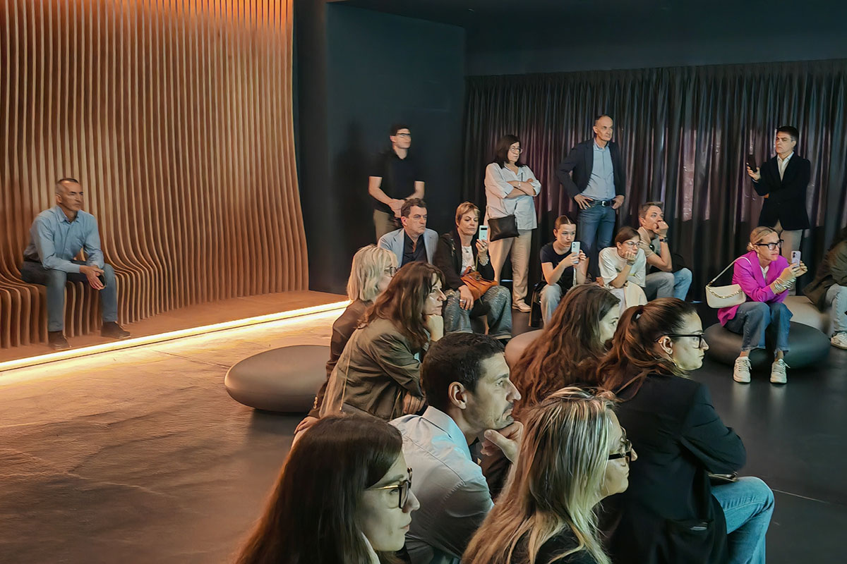 Pubblico seduto nella sala immersiva davanti alla parete parametrica in legno retroilluminata